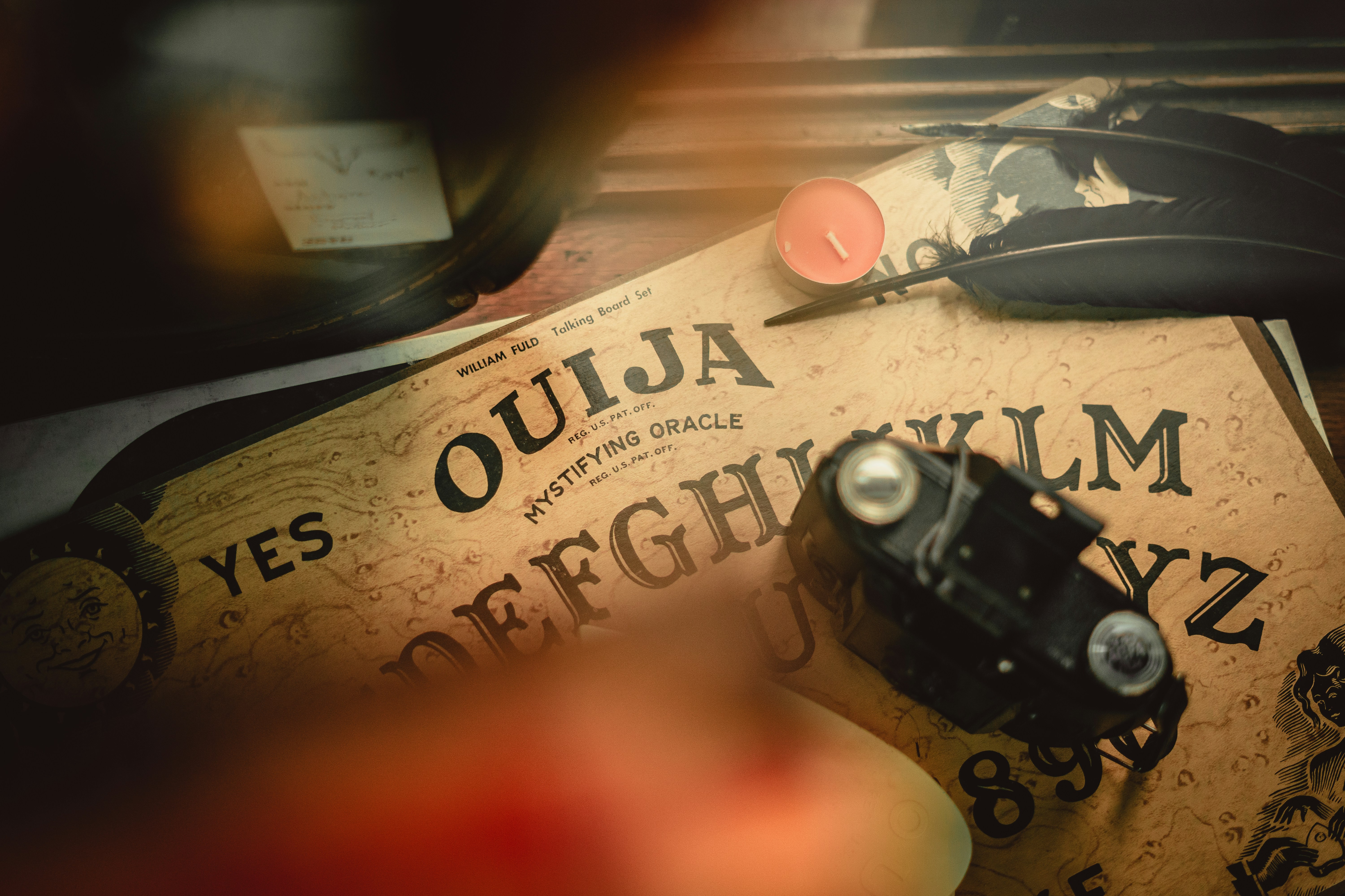 A Ouija board with black feathers and a reddish candle.